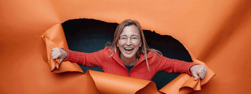 Leadership & culture expert Kim Scott breaks through an orange paper background